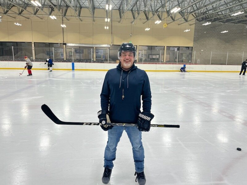 Mike standing on the ice in street clothes and a helmet