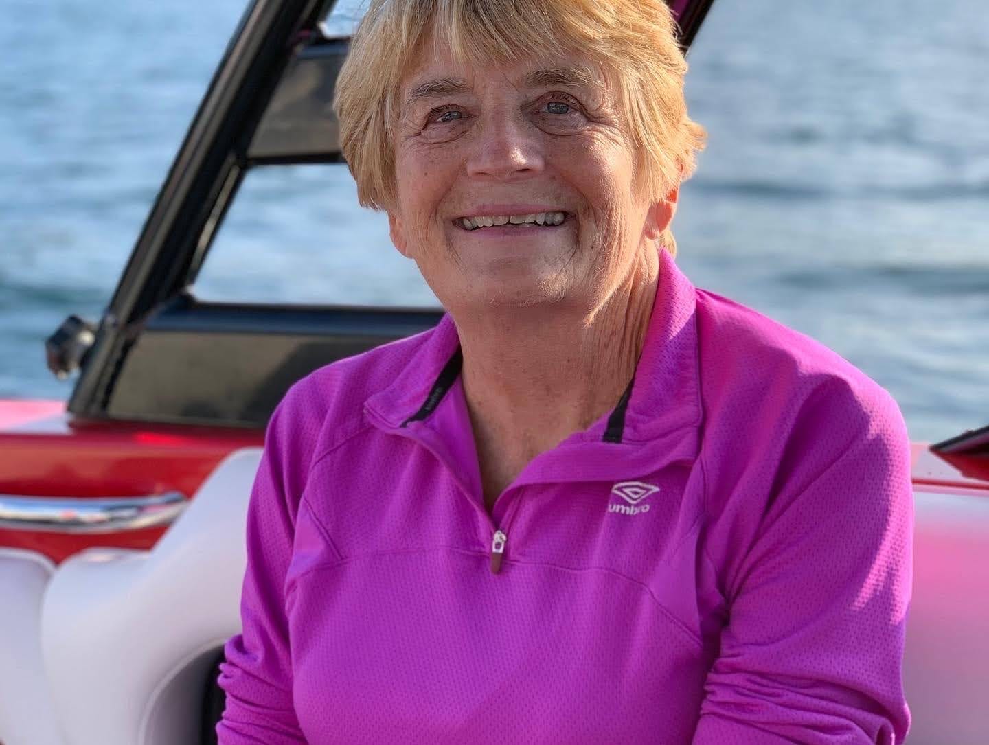 A smiling woman in a bright pink pullover sitting on a boat on the lake