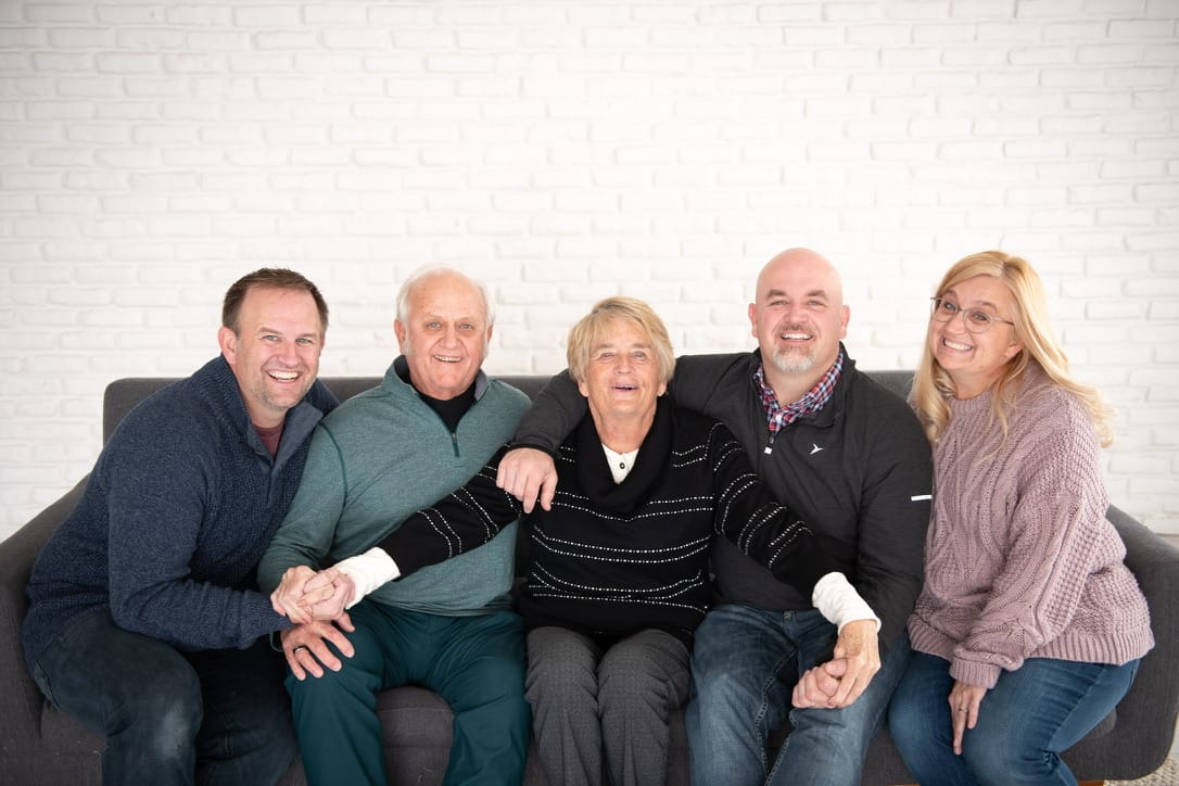 The Baker family together on a couch, laughing: Jon, Roger, Mom in the middle, Mike, and Jen.